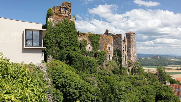 A castle ruin with a modern building adjacent to it, surrounded by lush greenery. -  Hôtel & Restaurant Origines par Adrien Descouls - Teritoria (Le Broc)