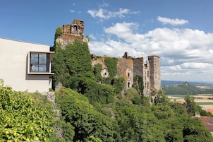 Ruinas de castillo con un edificio moderno adyacente, rodeado de vegetación exuberante.