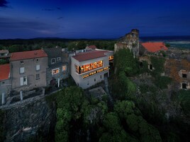Un edificio moderno con fachada de piedra y techo de tejas rojas, junto a una estructura histórica de piedra.