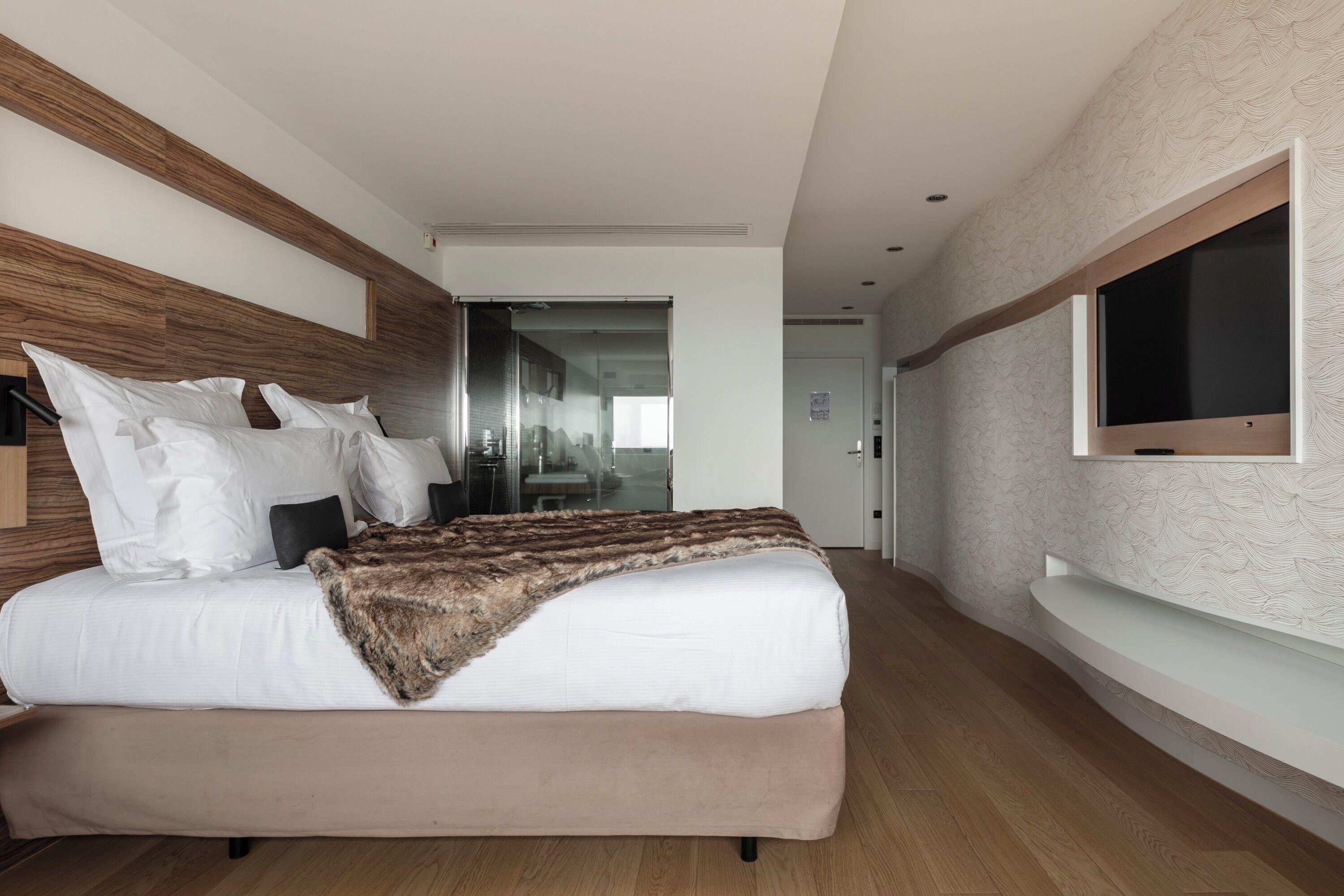 Una habitación de hotel moderna con una cama grande, un televisor montado en la pared y un cabecero de madera.
