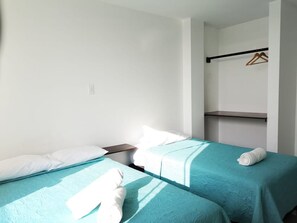 Habitación de hotel con dos camas individuales, una mesita de noche, un perchero y un estante.