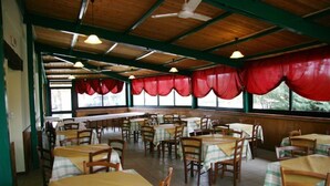 A restaurant with multiple tables and chairs, covered by a roof with red curtains, and large windows. - Il Campetto Country House (Senigallia)