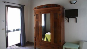 A room with a wooden wardrobe, a bed with a green bedspread, a small table, and a television on the wall. - Il Campetto Country House (Senigallia)