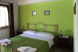 Een kamer met een groene wand, een houten bed met wit beddengoed, twee nachtkastjes met lampen en een raam met gordijnen.