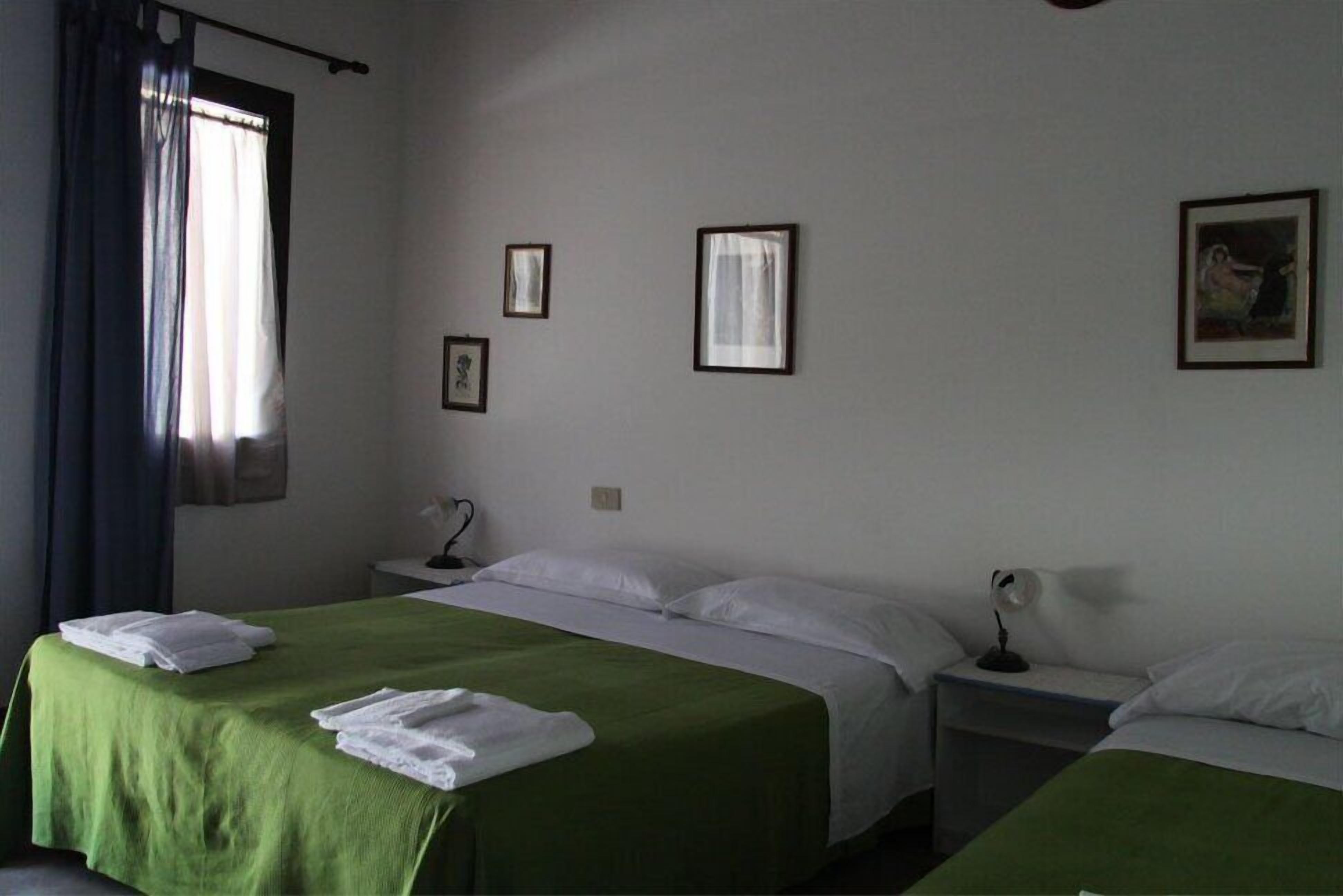 Habitació d'hotel amb dos llits, una tauleta de nit amb una làmpada i una finestra amb cortines.