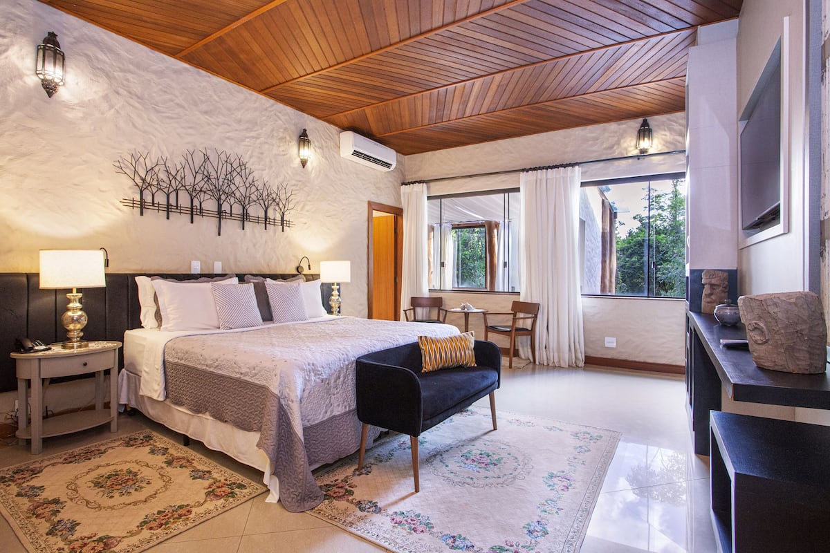 A bedroom with a bed, bedside tables, a bench, a desk, and a window with curtains.