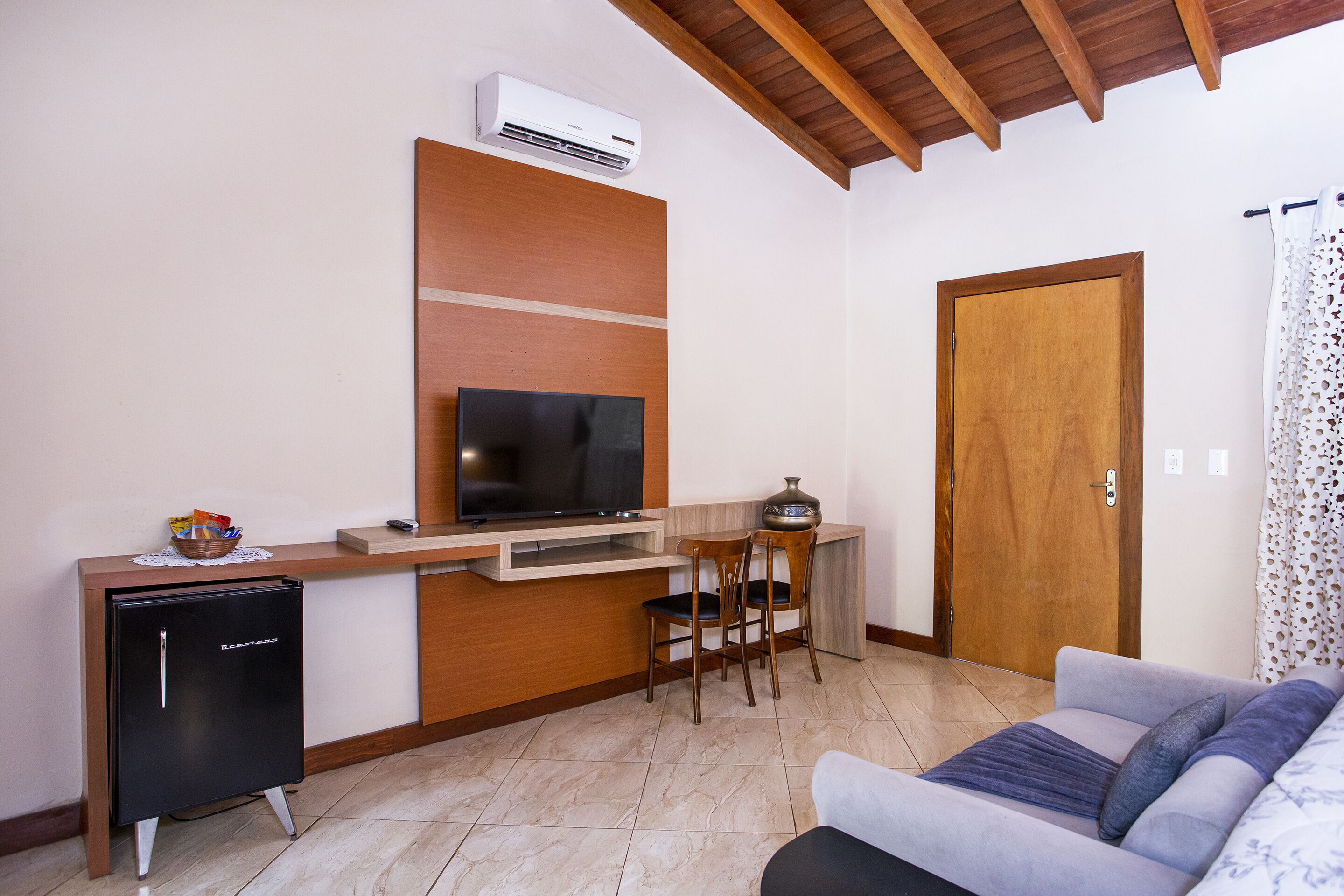 A compact living space with a kitchenette, a flat-screen TV, a refrigerator, a sofa, and a wooden door.