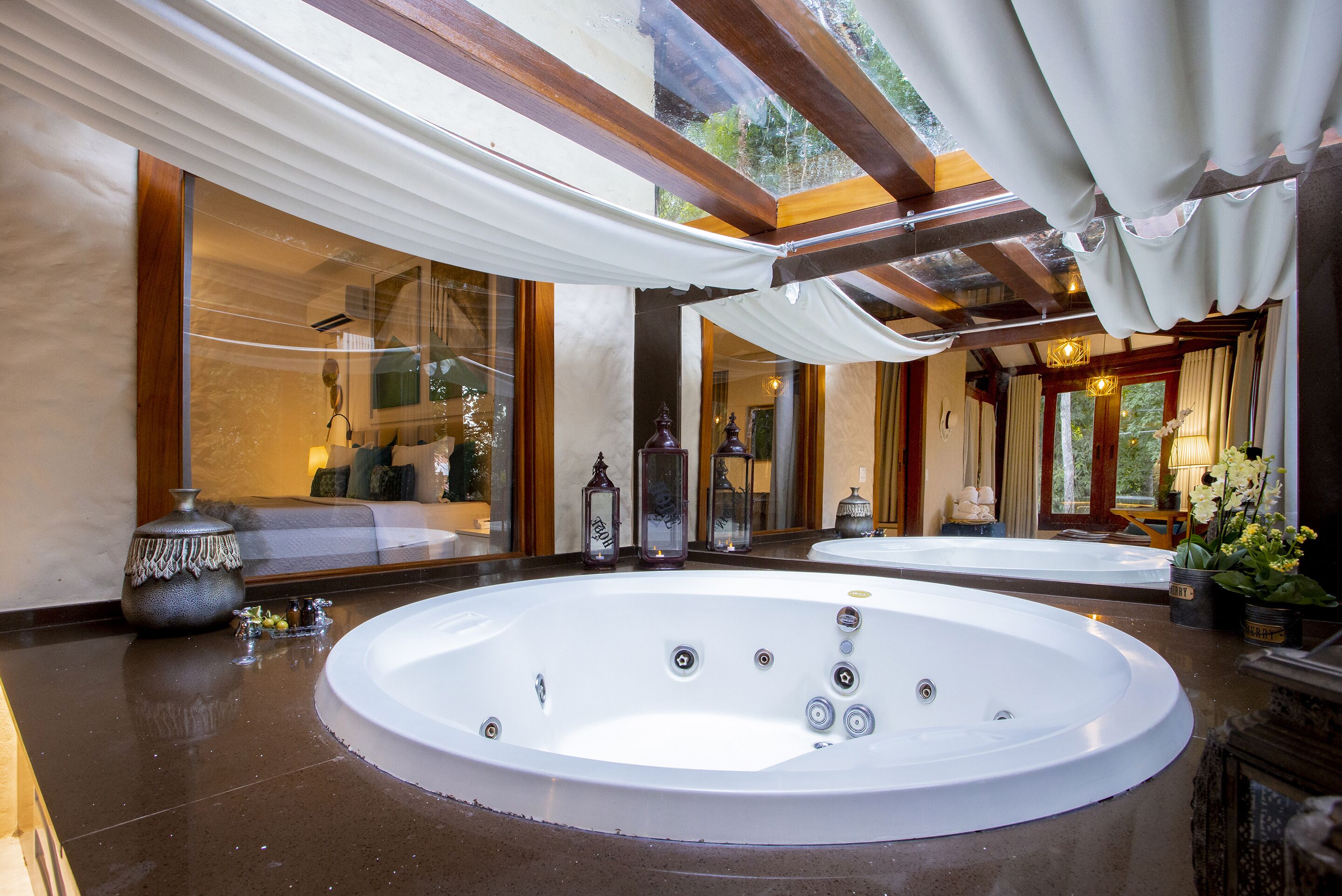 Een luxueus wellnessgedeelte met twee bubbelbaden, een grote spiegel en uitzicht op een tuin.
