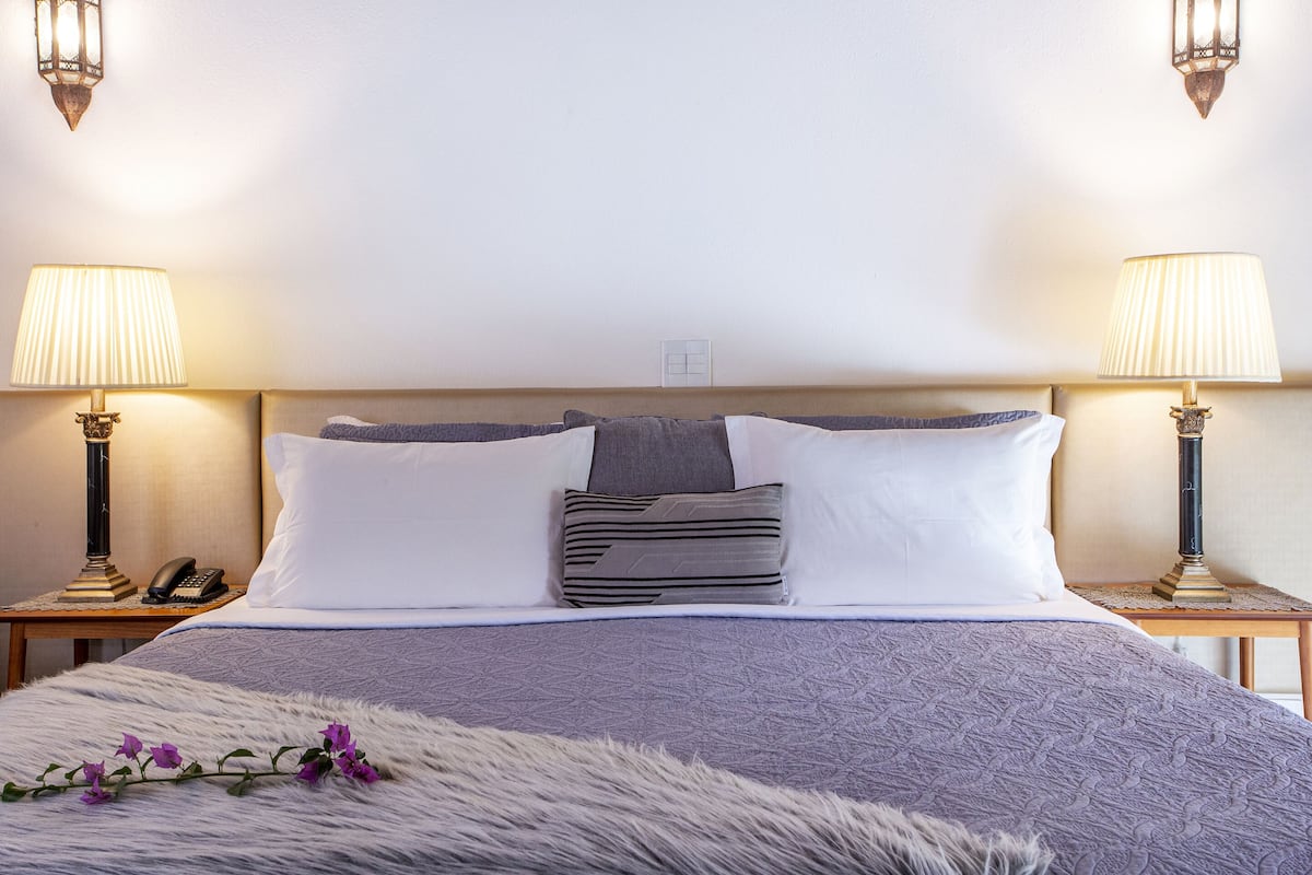 A neatly made bed with a fluffy white throw, two bedside lamps, and a telephone on a wooden nightstand.