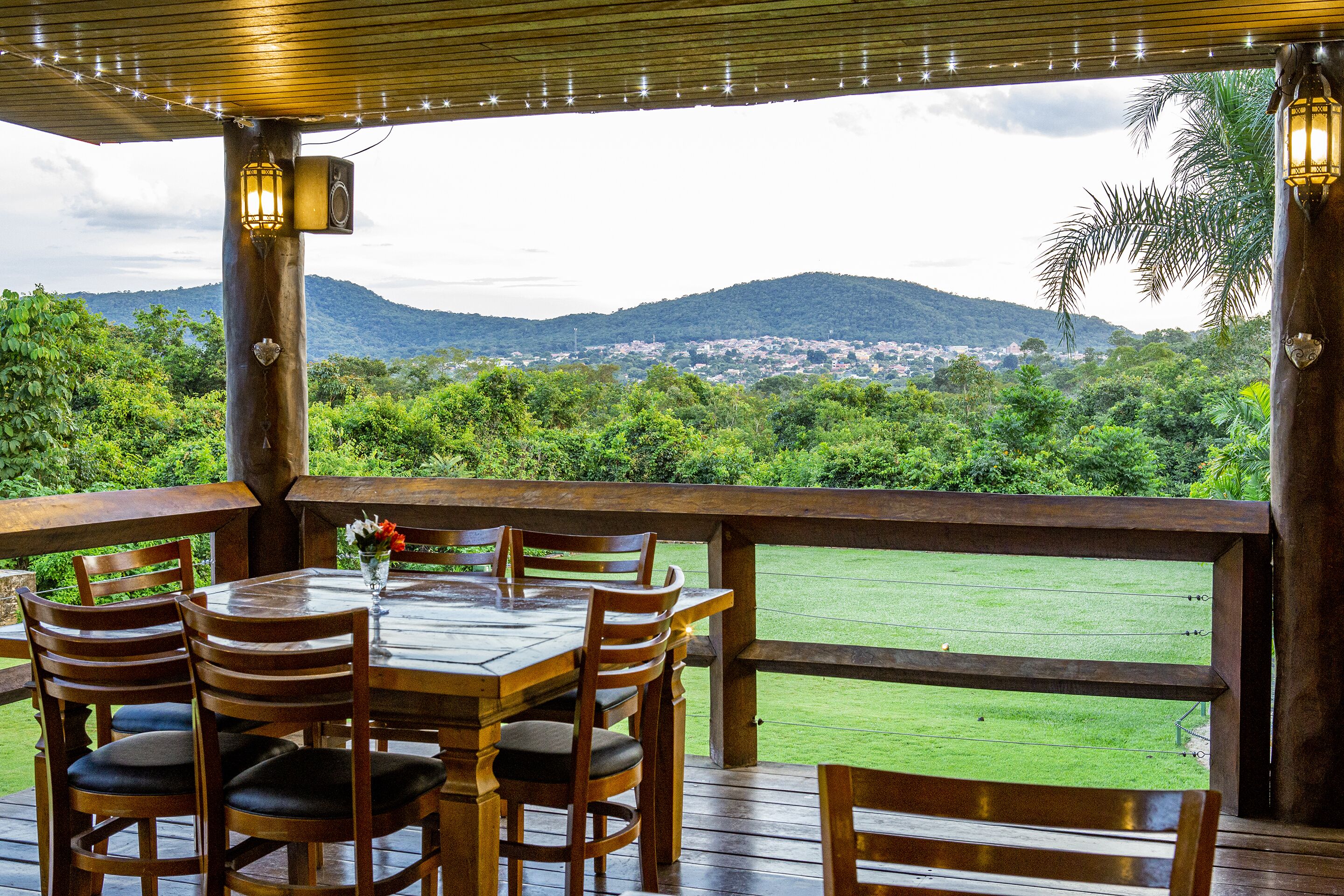 An outdoor wooden deck with a table and chairs, overlooking a lush green landscape and distant hills.
