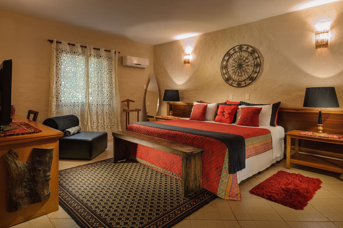 A bedroom with a bed, bedside tables, a desk, a chair, a mirror, and a wall decoration.
