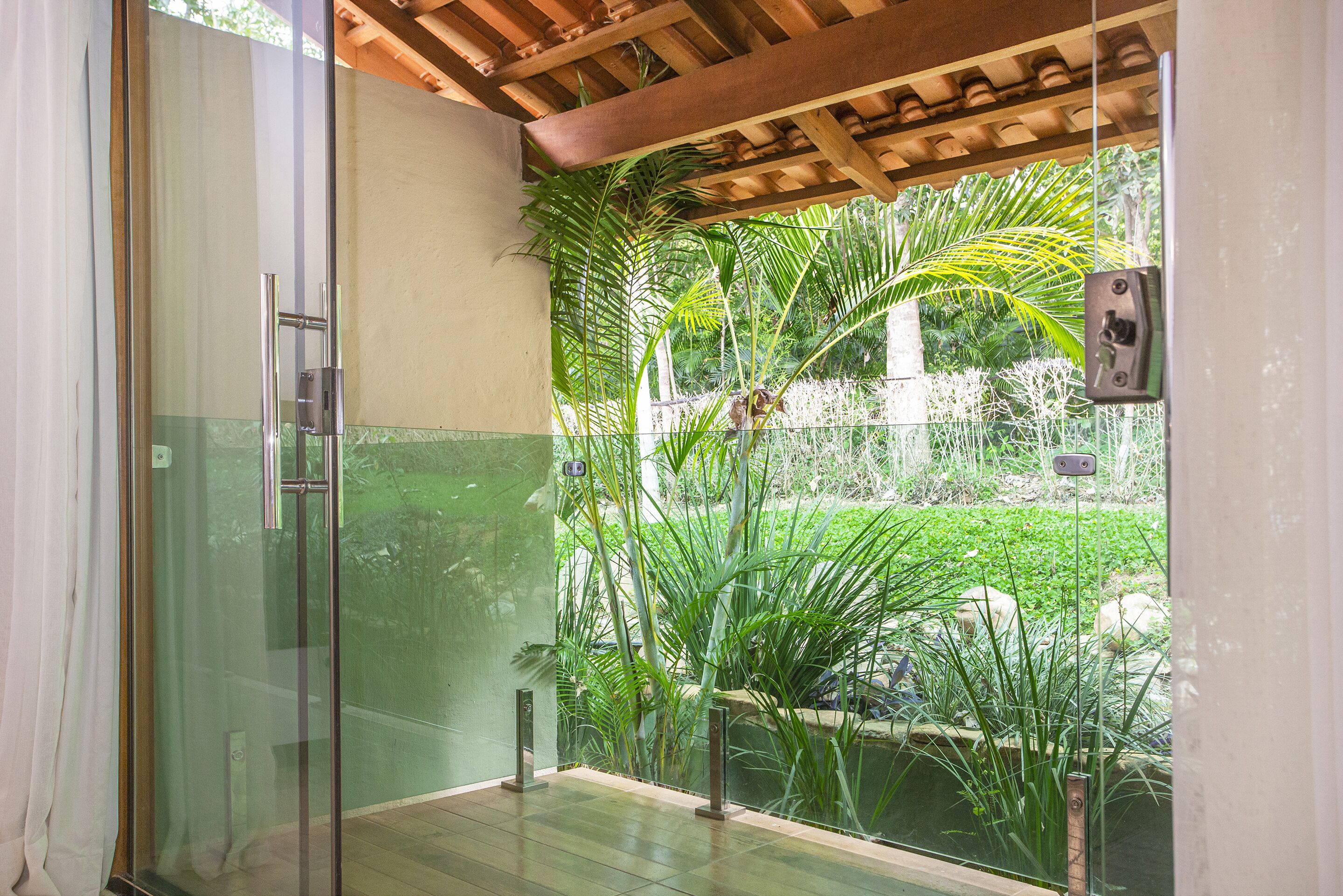 Zona de ducha con paredes de cristal, techo de madera y vistas a un jardín exuberante.