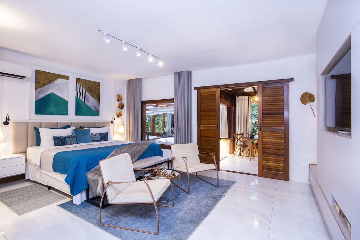 A modern bedroom with a large bed, a seating area, and a view of the outdoors.