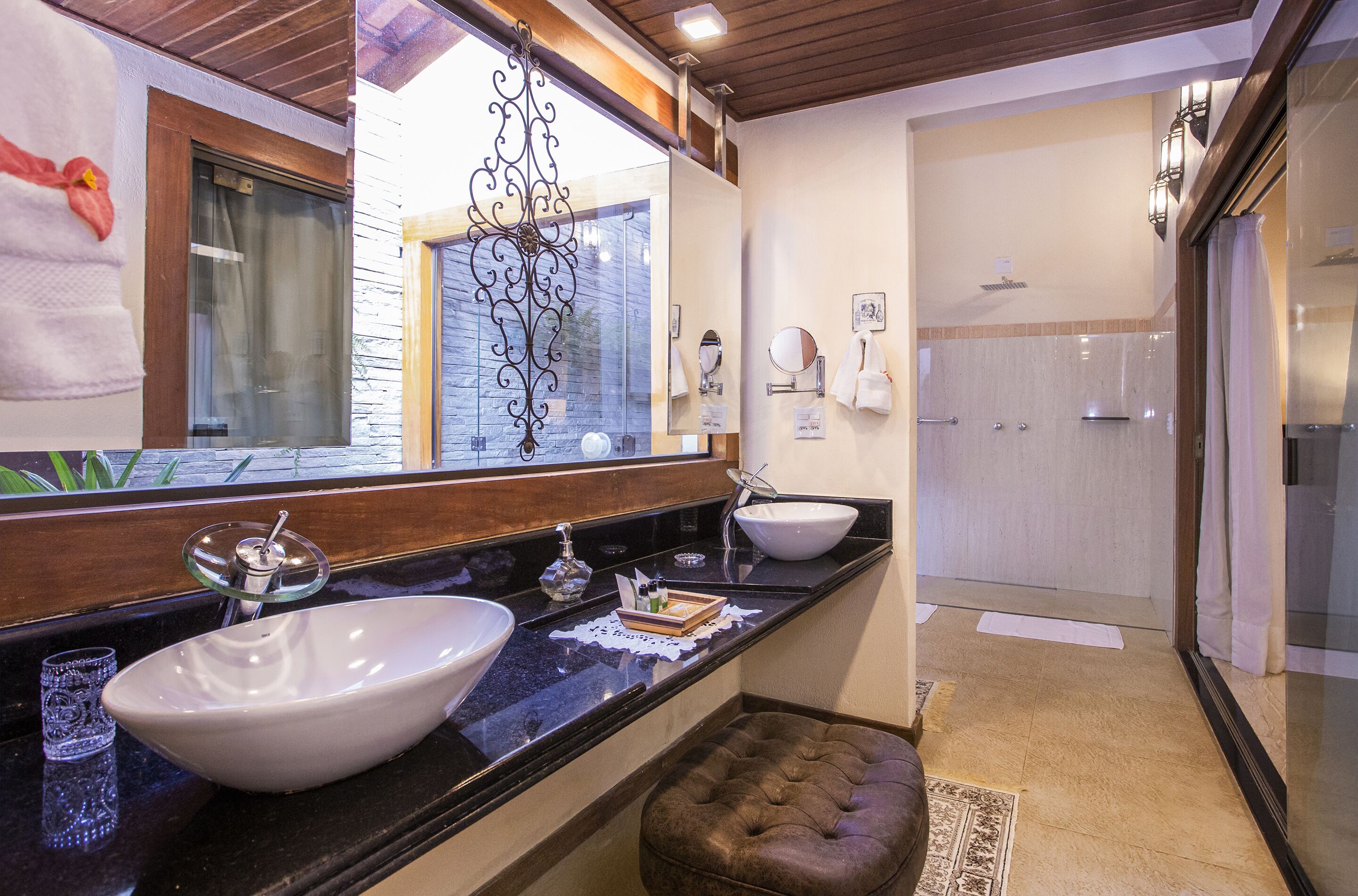 Un baño con un espejo grande, dos lavamanos, cabina de ducha de vidrio y techo de madera.