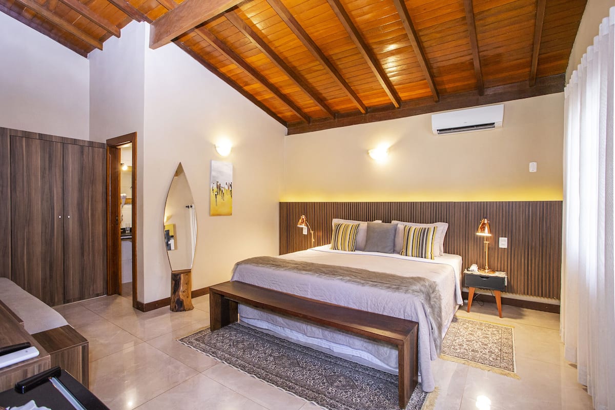 A bedroom with a wooden ceiling, a large bed with multiple pillows, bedside tables with lamps, and a bench.