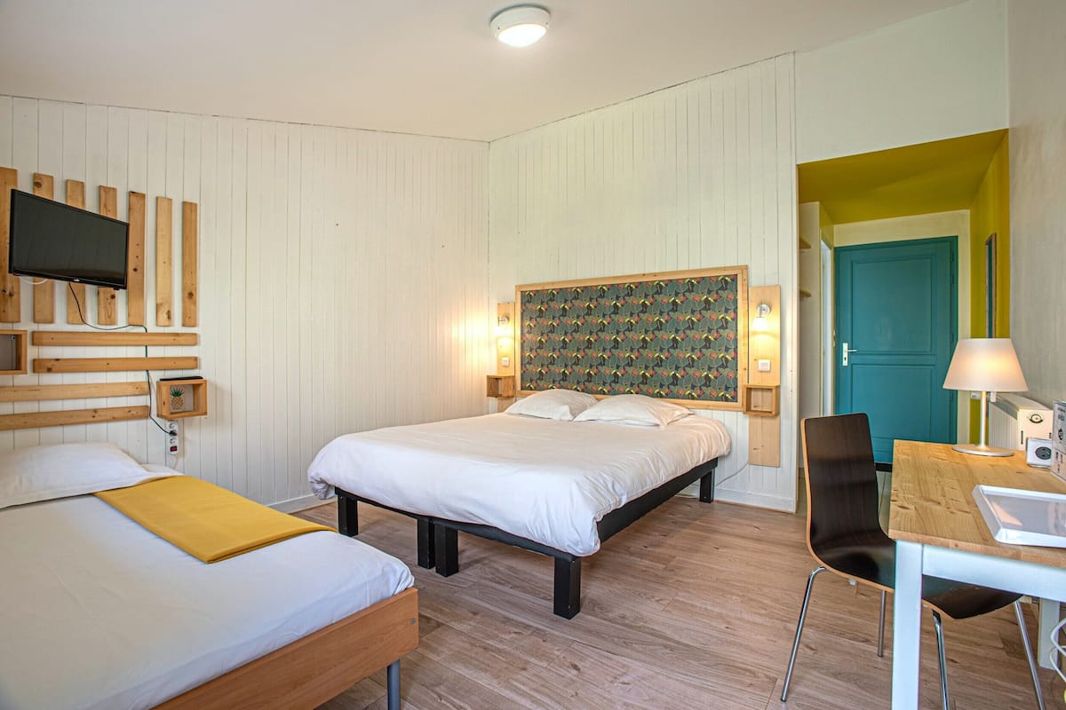 A hotel room with two beds, a TV, a desk with a lamp, and a door leading to another room.