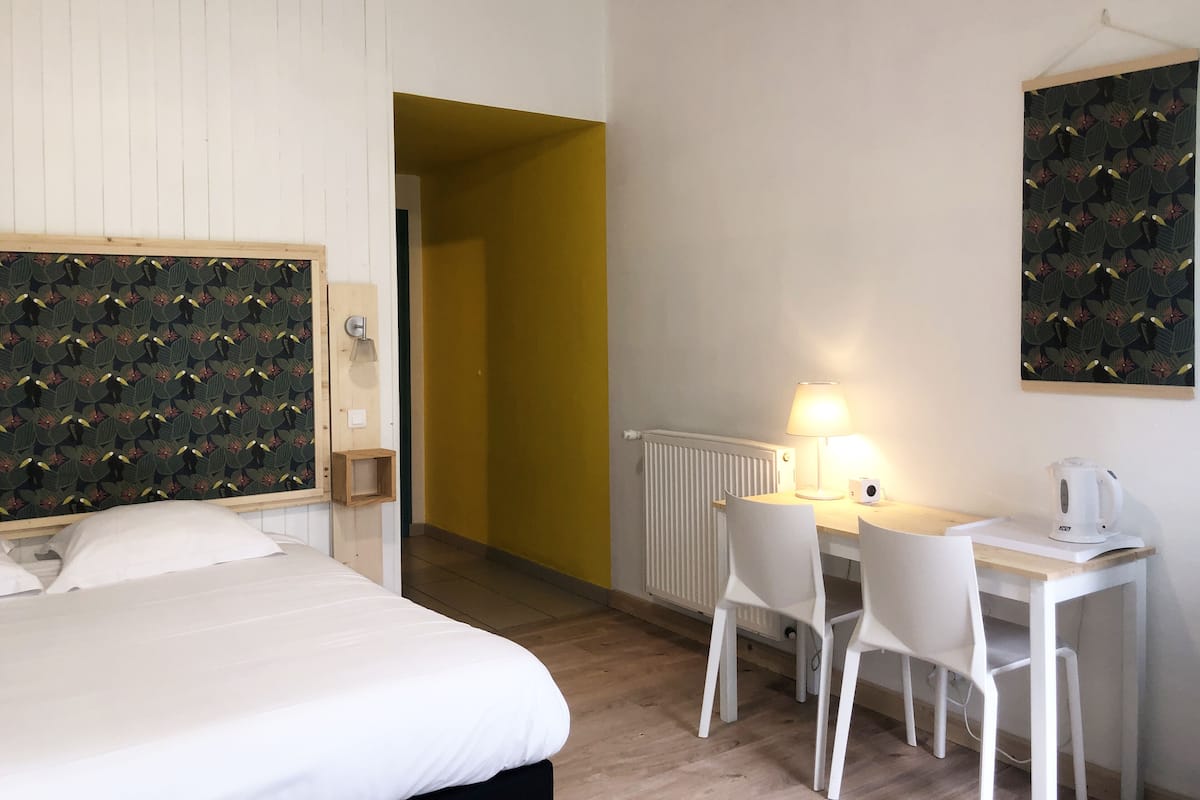 A hotel room with a bed, a desk, a chair, a lamp, and a radiator.