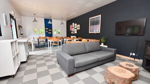 Et moderne opholdsområde med en grå sofa, træbænk, et fladskærms-tv og et spiseområde med stole og borde.