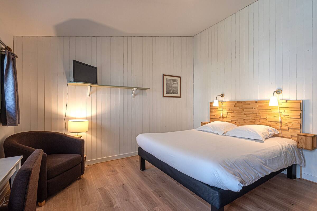 A bedroom with a bed, a chair, a TV mounted on the wall, and a framed picture.
