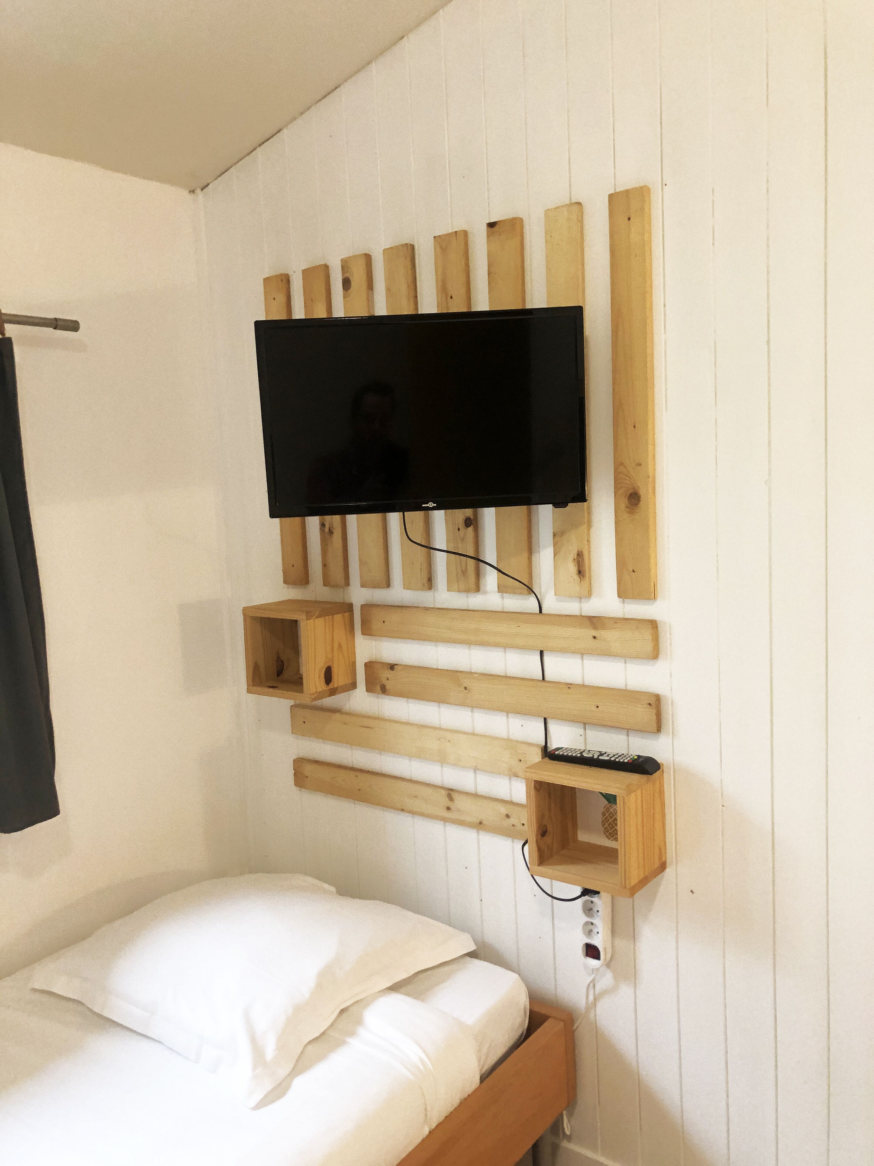A bedroom with a wooden slat wall, a mounted TV, a bed with white bedding, and a bedside table with a remote control.