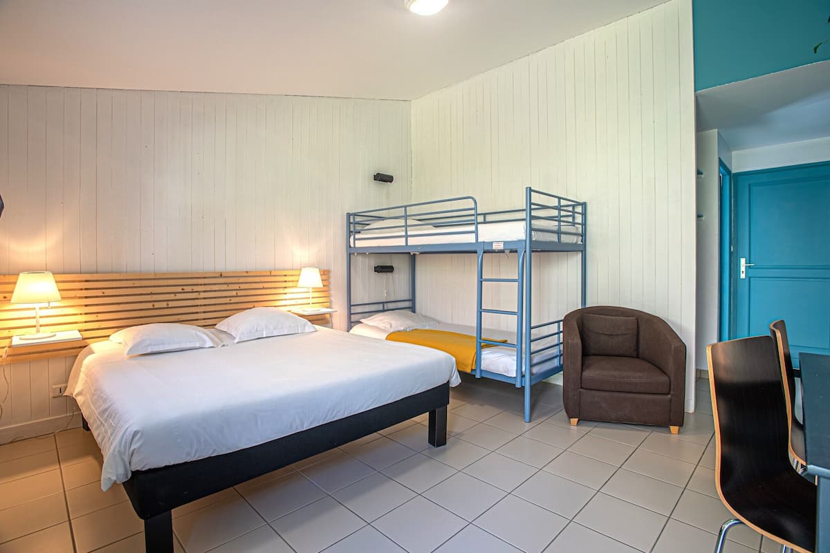 A room with a single bed, a bunk bed, a brown armchair, and a table with chairs.