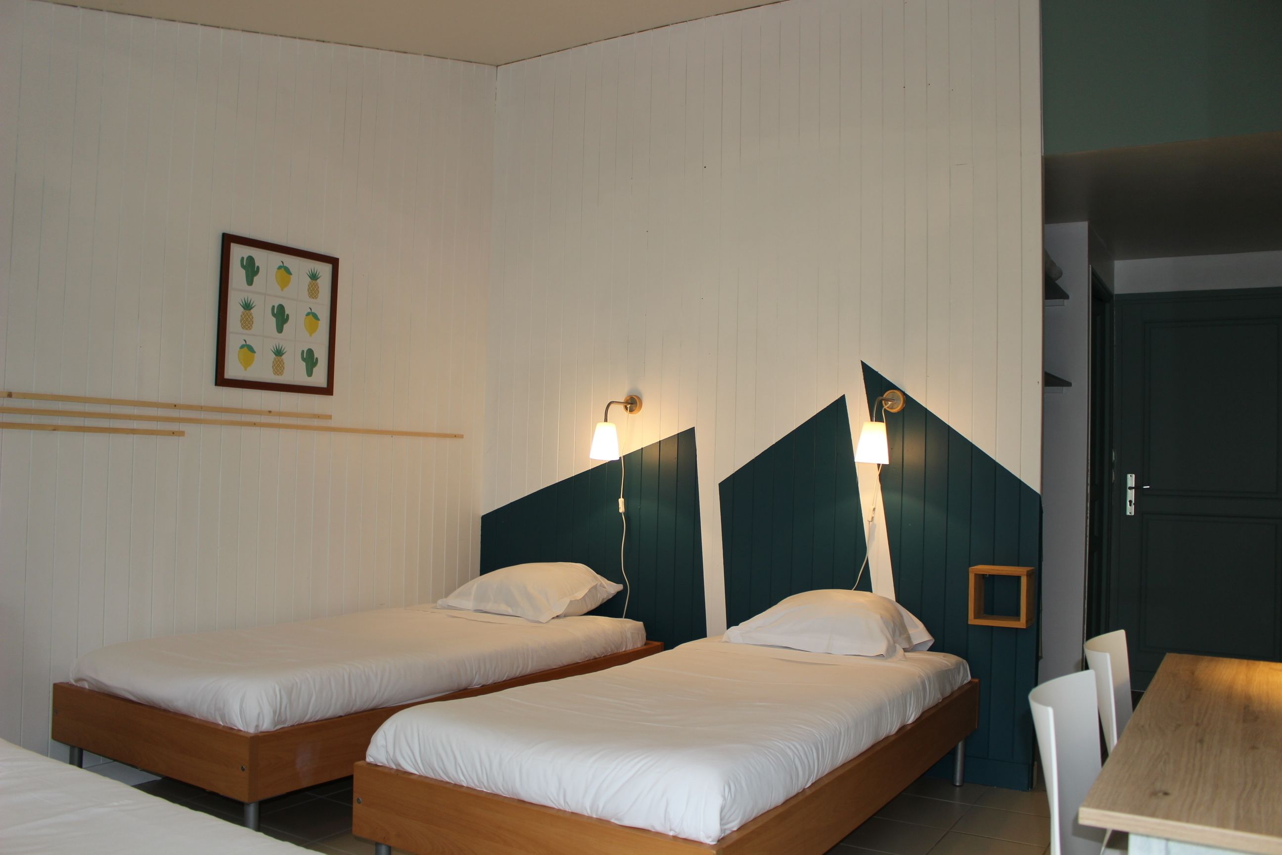 Ein Zimmer mit zwei Einzelbetten, einem Holztisch und einem gerahmten Bild an der Wand.