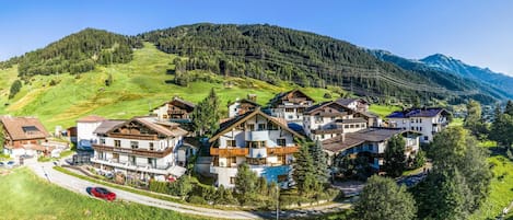 Ein Bergdorf mit traditionellen Chalets, einer kurvenreichen Straße und bewaldeten Hügeln im Hintergrund.