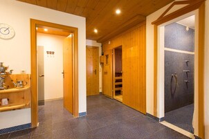 A hotel hallway with a wooden floor, a clock, a tea set, and a shower area.
