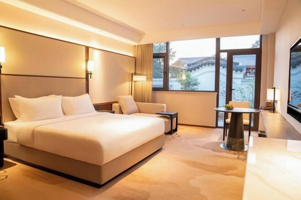 A hotel room with a large bed, a small table, and a view of a traditional building outside the window.
