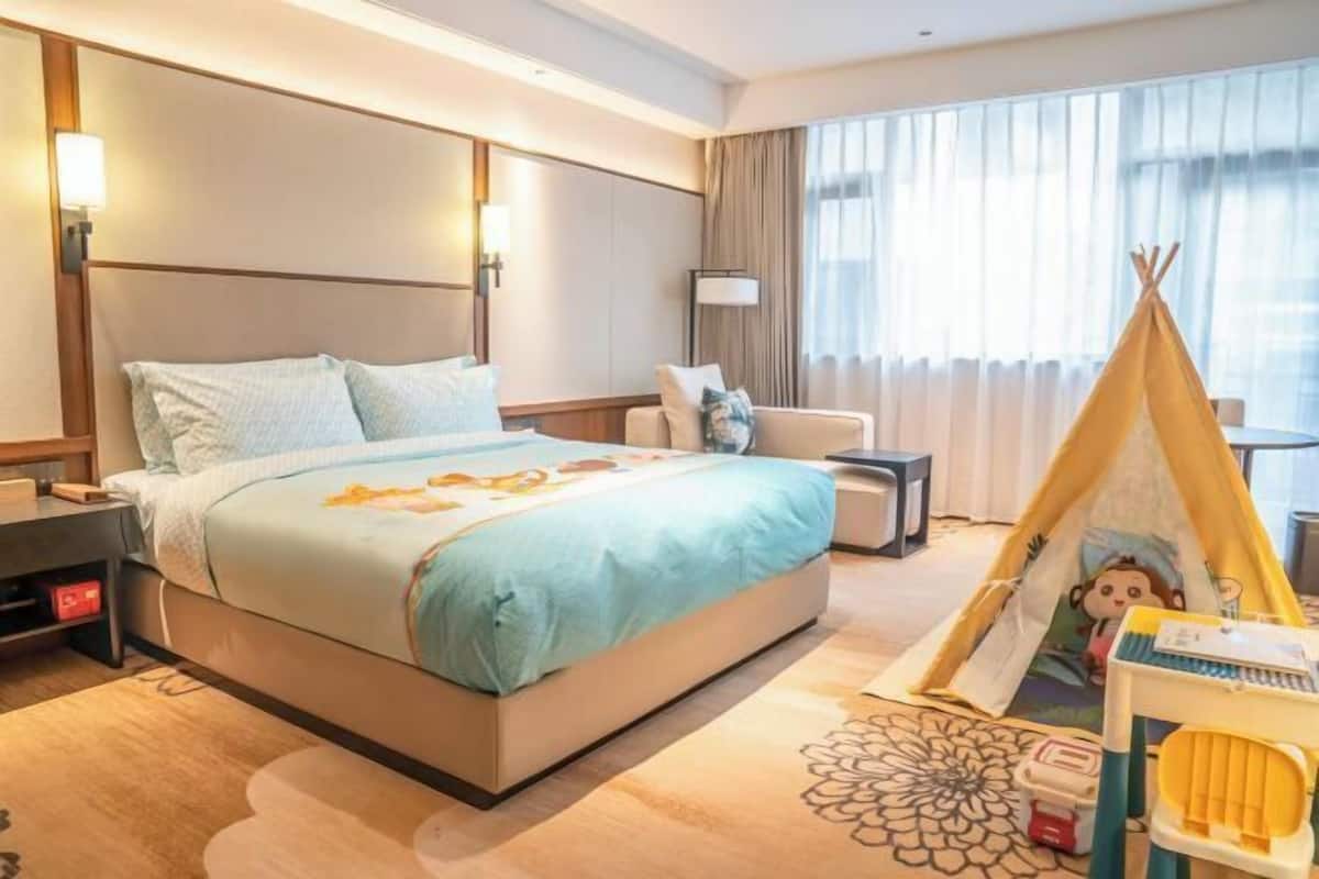 A hotel room with a bed, bedside tables, a lamp, a chair, a window with curtains, and a teepee decoration.