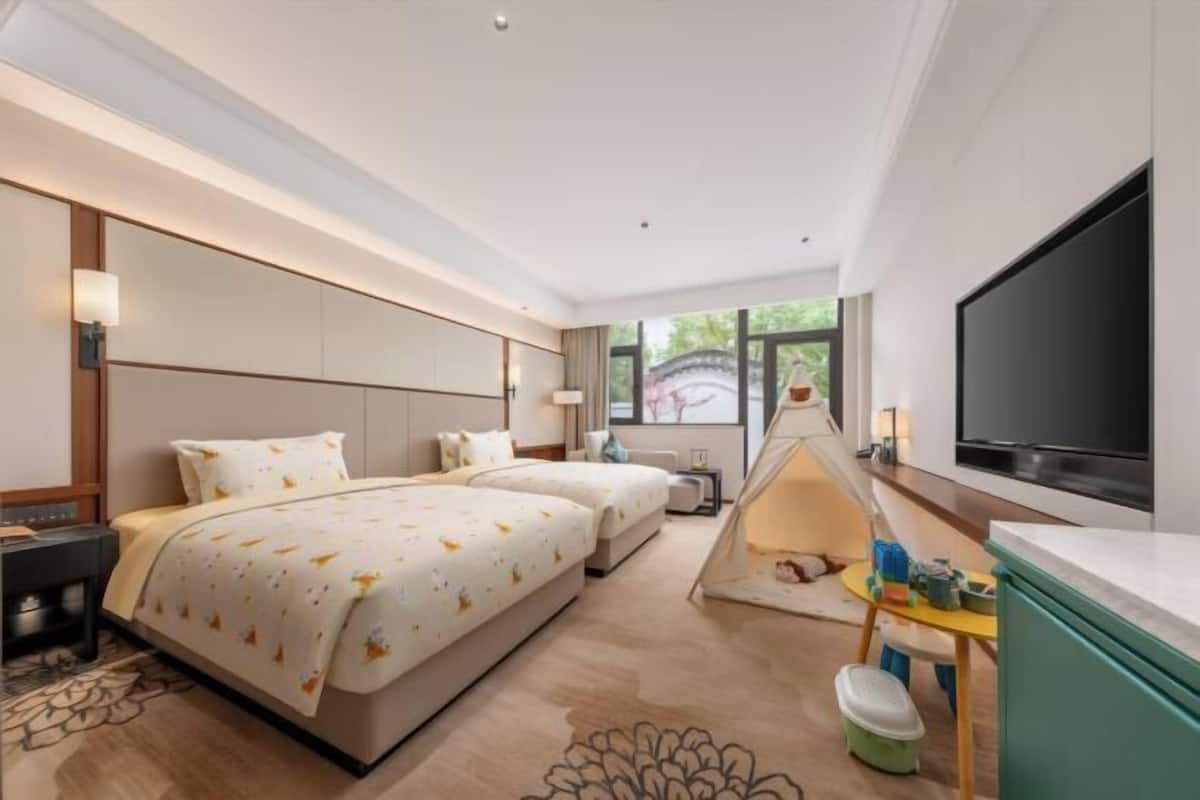 A hotel room with a bed, two bedside tables, a TV, a tent-like play area, and a window with a view.