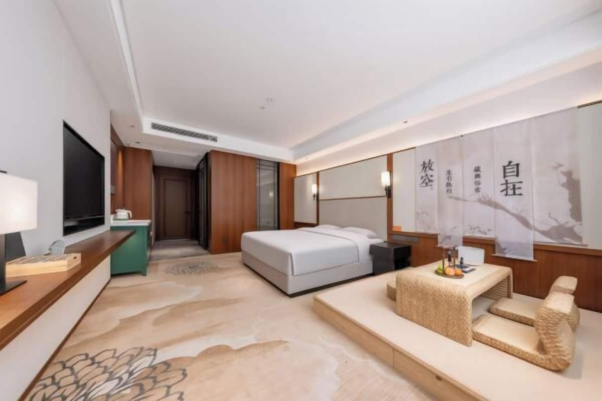 A hotel room with a bed, a desk, a TV, a sofa, and a wall with Chinese characters.