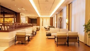 A hotel lobby with a long reception desk, several seating areas with chairs and sofas, and a large plant. - Good Fortune Hot Spring Hotel (Donghai)
