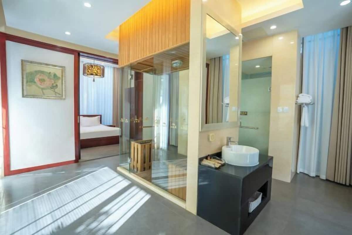 A modern hotel room with a large mirror, a bedside table, a built-in TV, and a small wooden stool.
