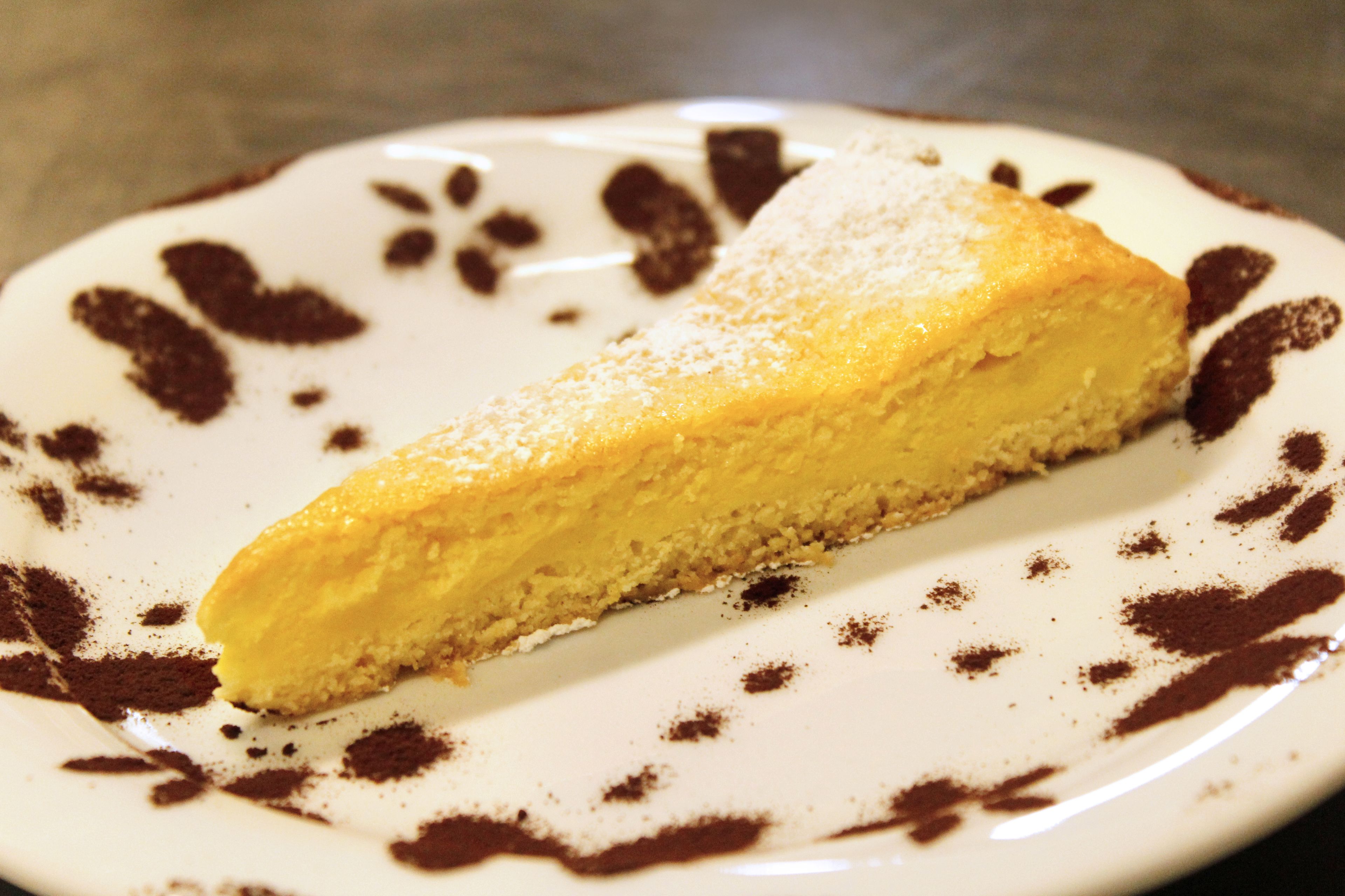 A slice of cheesecake on a plate with chocolate powder around it.