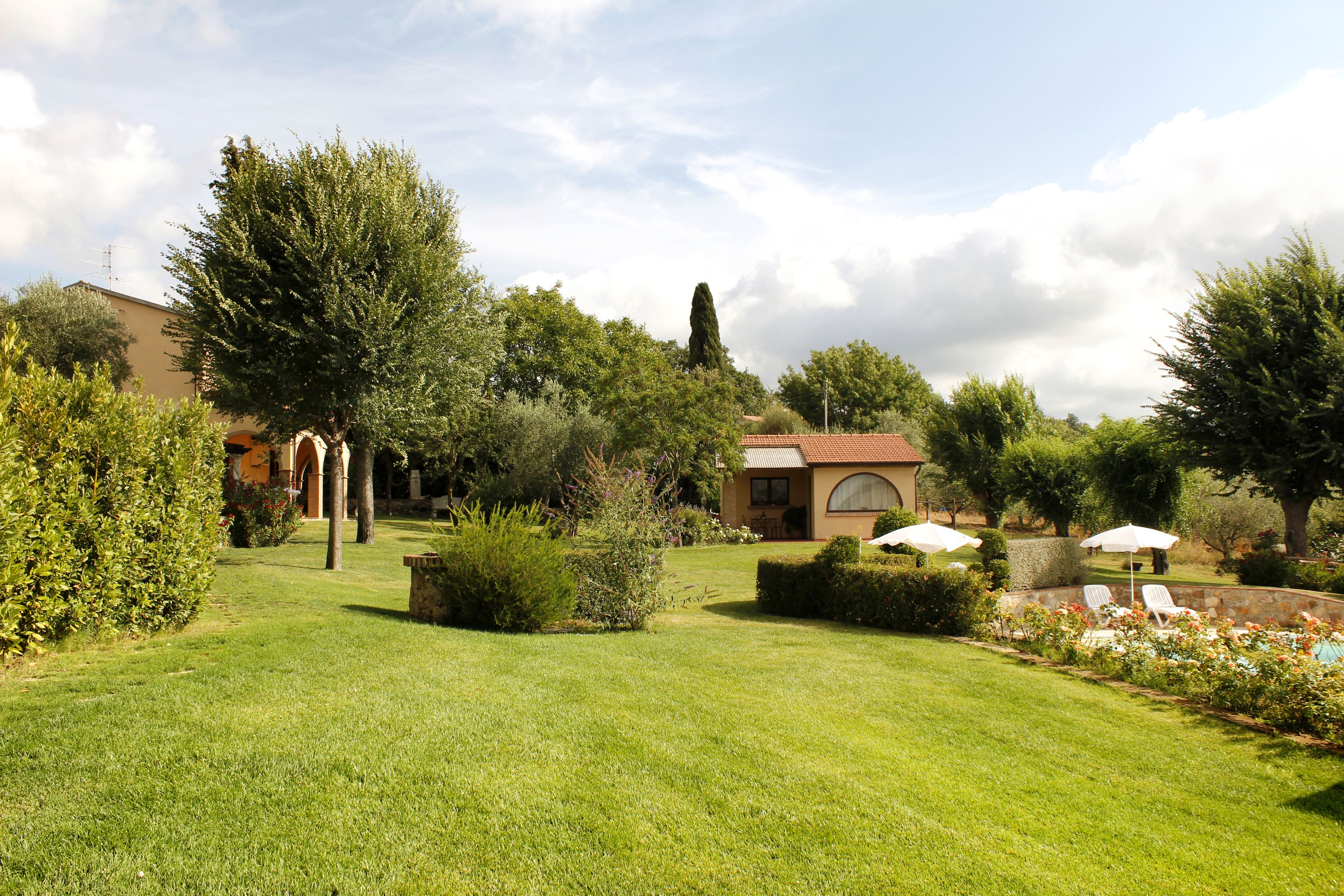A well-maintained garden with a lawn, various shrubs, and a building with a tiled roof.