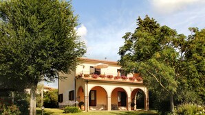 Uma casa de dois andares com jardim, entrada em arco e uma varanda florida.