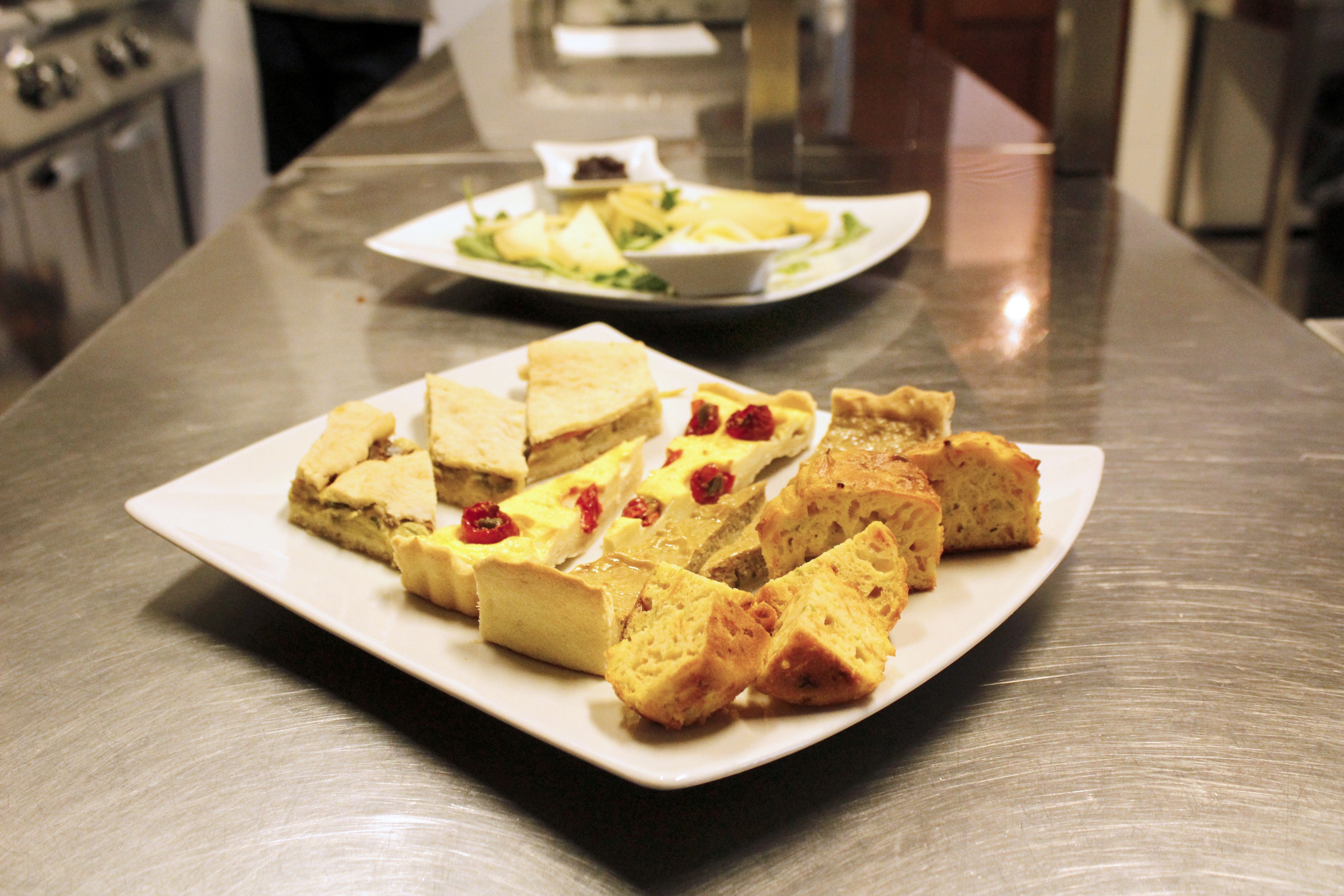 A stainless steel kitchen counter with a white plate of food, including various types of bread and a small bowl of salad.
