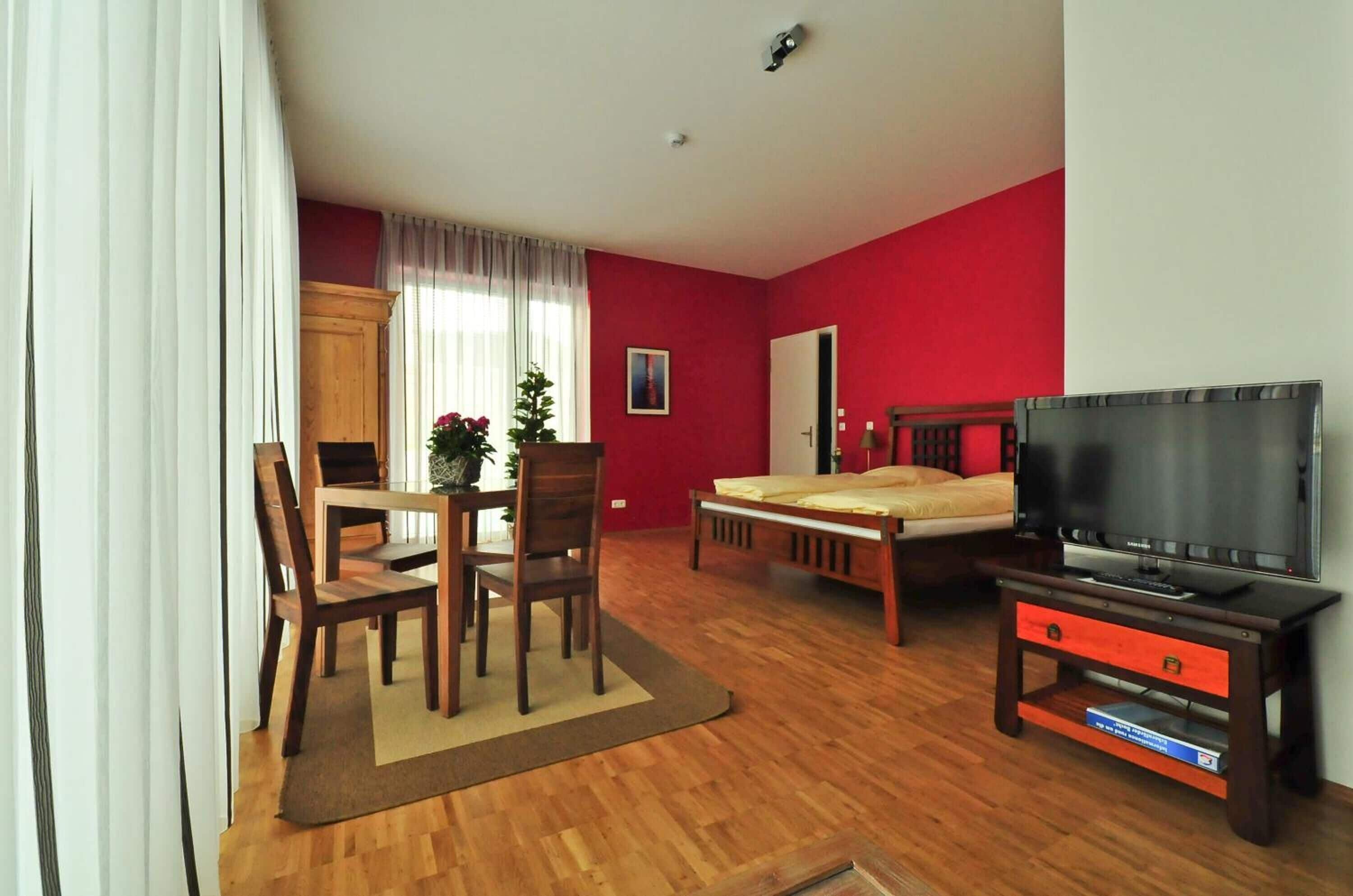 Una habitación con cama, televisor, una mesa de comedor con sillas y una planta pequeña.