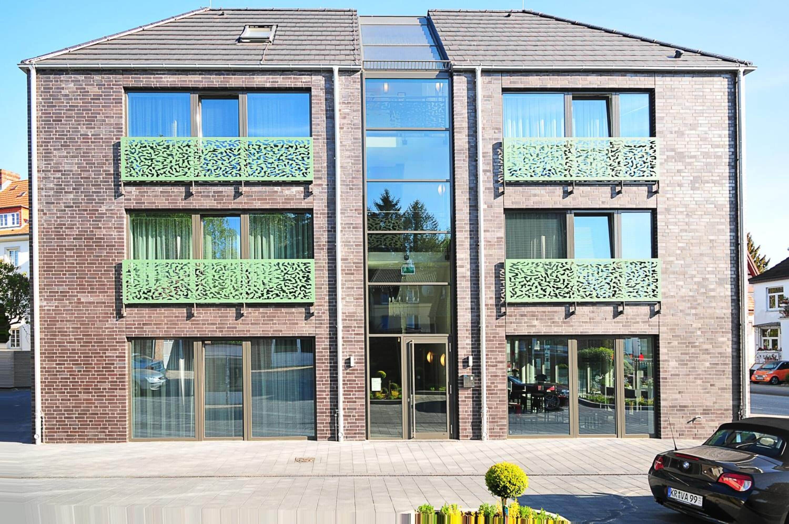 A modern two-story building with a brick facade, large windows, and decorative green lattice on the balconies.