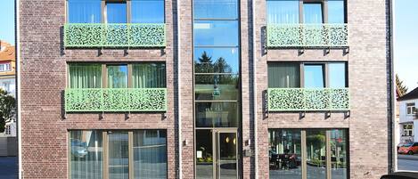 A modern two-story building with a brick facade, large windows, and decorative green lattice on the balconies.