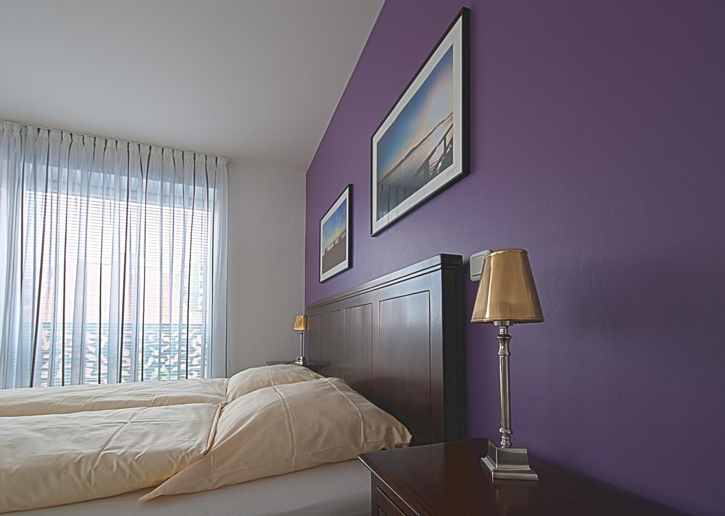 A hotel room with a bed, a nightstand, a lamp, and two framed pictures on the wall.