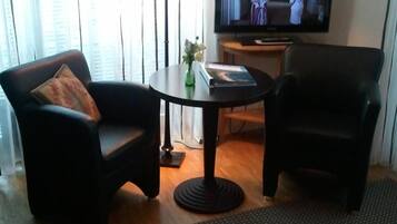Habitación de hotel con una cama, dos sillones, una mesita con lámpara, televisor y ventana con persianas.