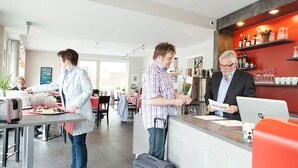 A hotel lobby with a reception desk, a bar area with shelves of bottles, and a dining area with tables and chairs.