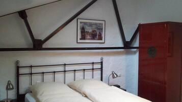 A single bed with a headboard, a bedside lamp, a nightstand, a red wardrobe, and a framed picture on the wall.