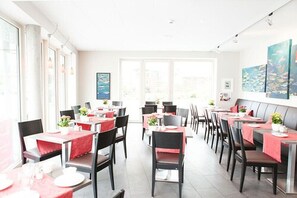 A restaurant with tables set for dining, chairs, and artwork on the walls. - Heldts Apartment-Hotel (Eckernfoerde)
