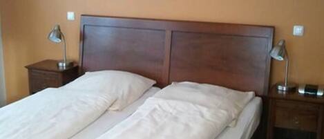Una cama doble con cabecera de madera, dos mesitas de noche con lámparas y dos cuadros enmarcados en la pared.