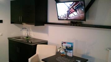 Una kitchenette compacta con un lavamanos, armarios y un televisor montado en la pared.