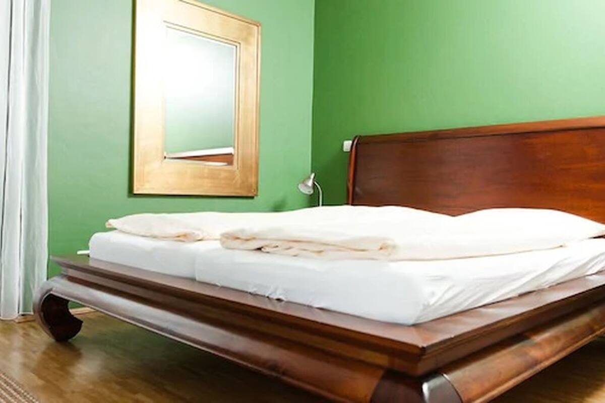 A neatly made bed with white linens in a room with green walls and a wooden headboard.