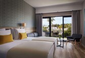 A hotel room with two beds, a desk, a chair, and a balcony with a view.